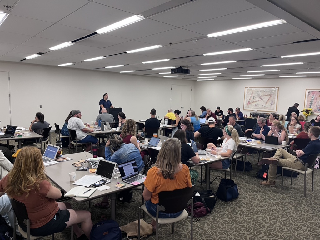 People in classroom at tables listening to presenter